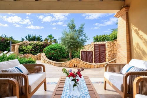 Luxurious patio at Top Villas Sardinia with rattan seating, blooming flowers, and stone walls overlooking gardens