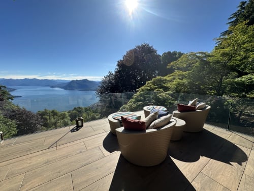 Terrazza lussuosa in riva al lago con arredamenti di design che si affaccia sul Lago Maggiore, Stresa, con montagne e vegetazione rigogliosa