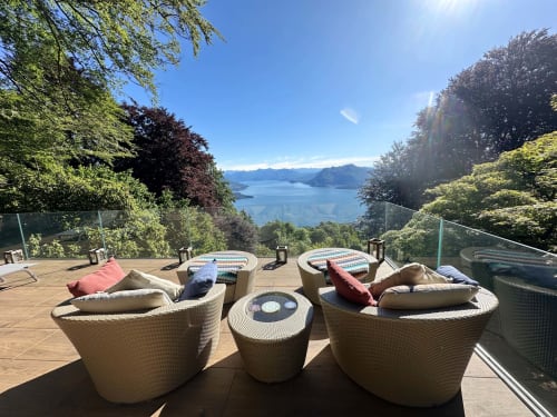 Terrazza di lusso affacciata sul Lago Maggiore con sedie in vimini, lettini e vedute panoramiche delle montagne e del lago