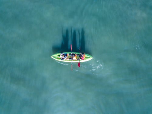 Vue aérienne d'un kayak vert avec trois pagayeurs dans les eaux turquoise près d'Uturoa, Polynésie française