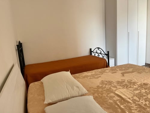 Camera da letto con letto in ferro battuto, cuscini color crema su biancheria beige decorata e plaid arancione in My Home Apulia