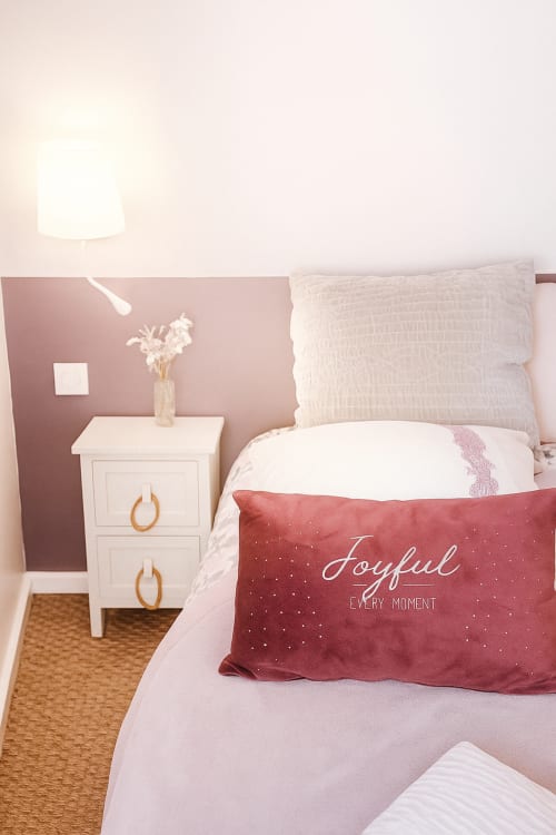Chambre pastel au Maunoury Citybreak Chartres avec murs rose, table de nuit blanche, coussin bordeaux et décoration moderne