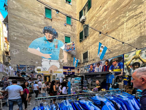 Street market with Maradona mural, blue jerseys, and flags in Naples near Suite Maradona B&B