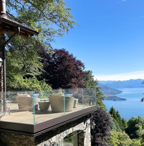 Terrazza lussuosa sul lago con sedie in vimini che si affacciano sul Lago Maggiore, Italia, con vista sulle montagne e balaustre in vetro
