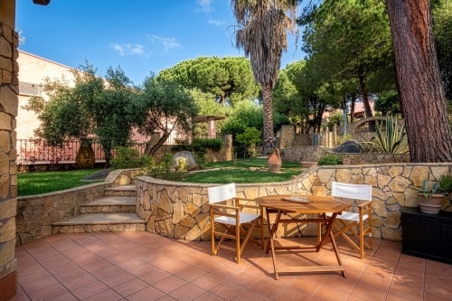 Terracotta patio with wooden dining table at Top Villas Sardinia, featuring stone walls and lush Mediterranean gardens