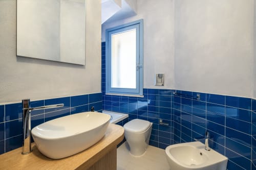 Modern bathroom at Top Villas Sardinia with blue tile walls, wooden vanity, freestanding white tub, and toilet in Quartu