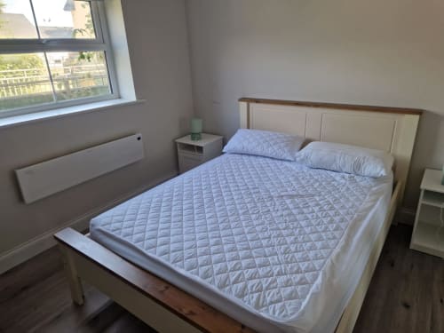 Bright bedroom at Boswell Equestrian Centre with queen bed, white linens, pillows, nightstand, and window view in Ashford
