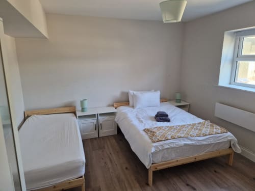 Bright bedroom with two single beds, wooden frames, white linens, shared nightstand, and window at Boswell Equestrian Centre,