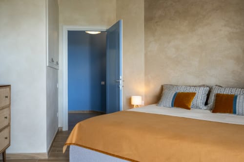 Modern bedroom at Top Villas Sardinia with orange throw, patterned pillows, and open blue door to ensuite