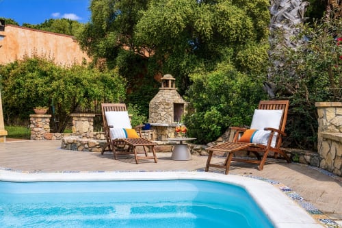 Luxurious pool area at Top Villas Sardinia with lounge chairs, stone fireplace, and lush greenery in Quartu Sant'Elena