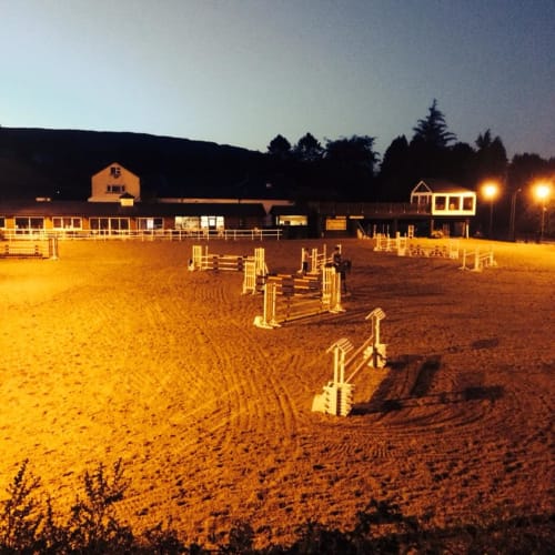 Boswell Equestrian Centre in Ashford at dusk, featuring a lit sand arena with jump obstacles and facilities buildings