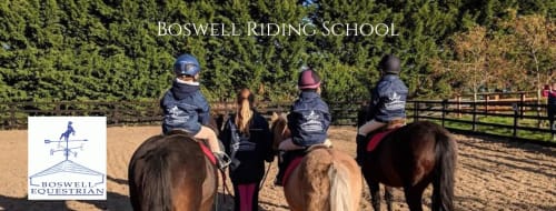 Boswell Riding School instructors teaching students on horses in arena with woodland backdrop