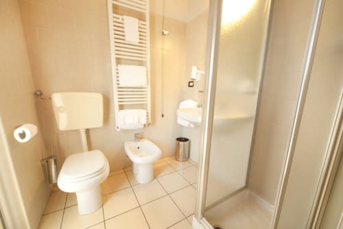 Modern bathroom at Agorà Calamandrana hotel with toilet, bidet, sink, towel rack, and walk-in shower with glass enclosure