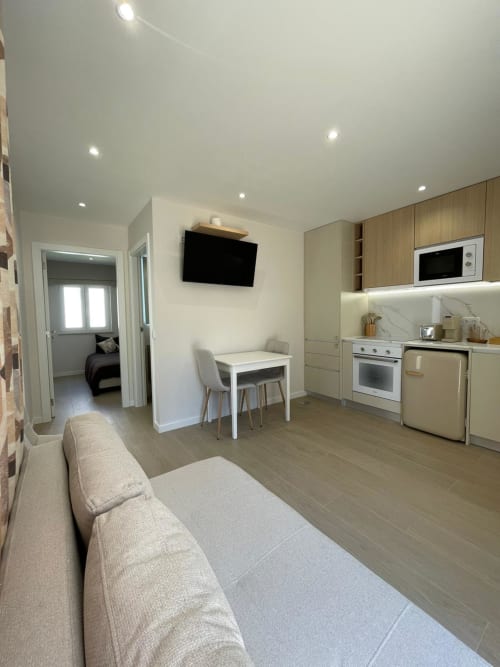Apartamento moderno em Vila Sotto Mayor, Figueira da Foz: sala com sofá, cozinha, mesa de jantar, TV e entrada do quarto