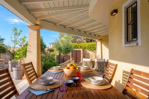 Shaded terrace dining area at Villa Tigli in Sardinia with wooden furniture, table settings, and sea views
