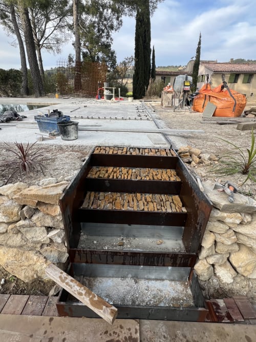 Foyer extérieur en construction à Mas Misajail, Le Castellet, avec grilles métalliques rouillées et encadrement en pierre