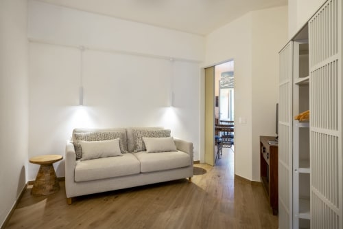 Modern villa living room with beige sofa, pendant lights, wooden flooring, and sea view access in Sardinia