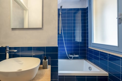 Modern bathroom in Villa Tigli with blue tiled walls, white bathtub, round vessel sink, and window at Top Villas Sardinia