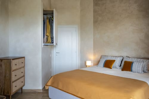 Modern bedroom in Villa Tigli, Sardinia with yellow bedding, wooden dresser, wall wardrobe, and white door