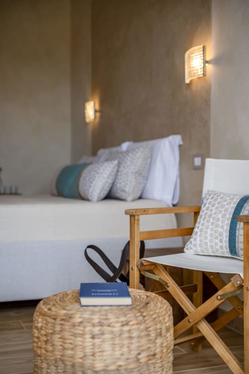 Bright villa bedroom at Top Villas Sardinia with wooden chair, wicker ottoman, and bed with patterned pillows and sea view in