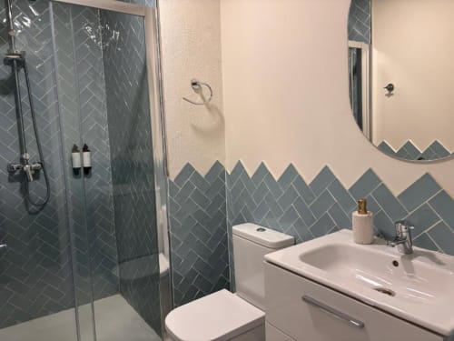 Baño moderno con azulejos en espiga gris, vanidor blanco, inodoro, ducha walk-in y espejo redondo en Top Home Integra