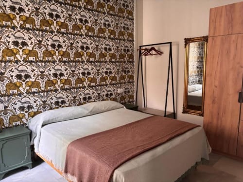 Habitación espaciosa con papel tapiz de vida silvestre estampado, cama queen con manta color óxido, armario de madera y espejo decorativo