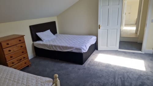 Bright attic bedroom at Boswell Equestrian Centre with black bed, wooden dresser, and gray carpet
