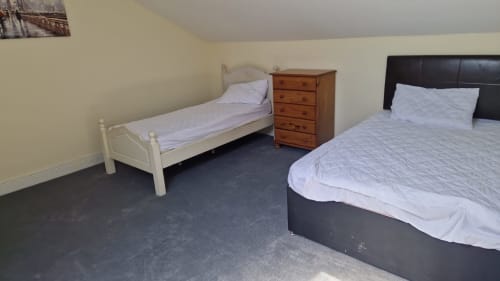 Bedroom at Boswell Equestrian Centre with white single bed, black double bed, wooden dresser, and grey carpet flooring.
