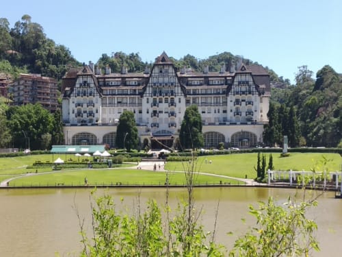 Grande hotel branco com estrutura de madeira aparente dominando os jardins e gramados à beira do rio no Rio de Janeiro