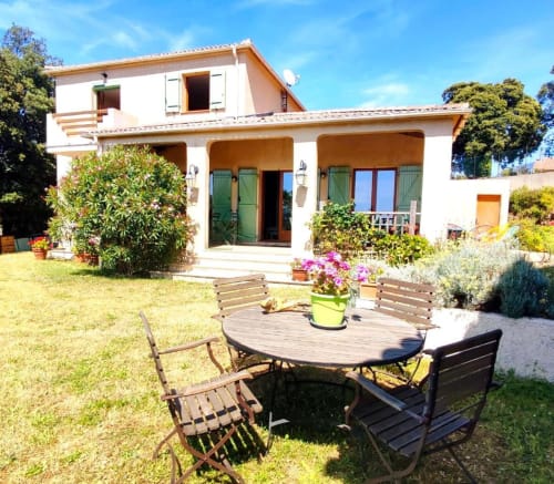 Cour du gîte Mare e Monti Vico avec table ronde, chaises, plantes fleuries et villa méditerranéenne chaulée