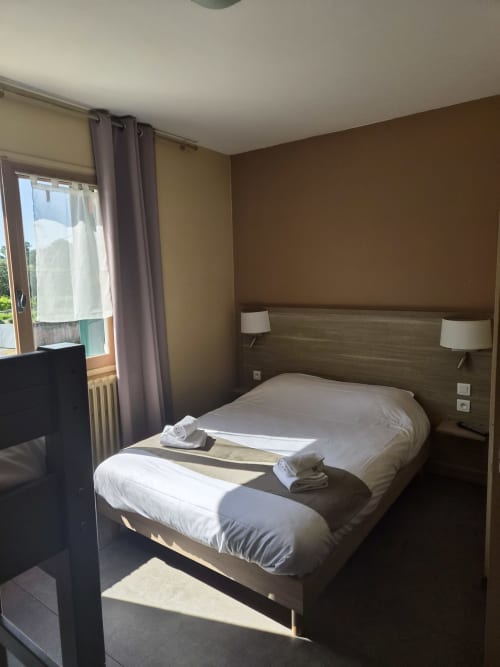 Chambre lumineuse à l'Hôtel Bar La Pinède avec lit queen, tête de lit marron, linge blanc et vue sur le jardin