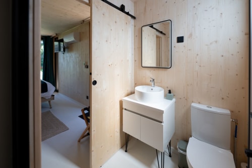 Modern bathroom with light wood walls, white vanity, and mirror at Le chant des pins Lodges, Saint-Marc-Jaumegarde