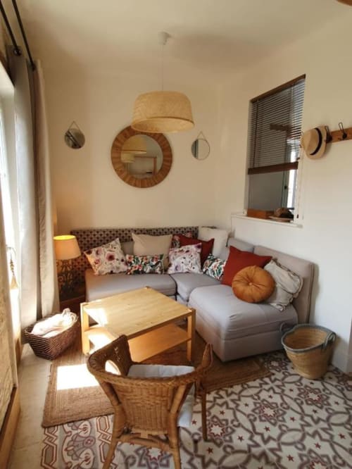 Salon chaleureux d'un appartement provençal avec canapé gris, table basse en bois, lampe suspendue tissée et miroirs décoratifs