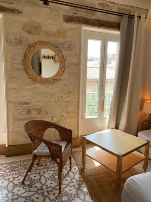 Chambre provençale authentique avec miroir rond tressé, fauteuil en rotin, table en bois et portes-fenêtres surplombant Châteaurenard