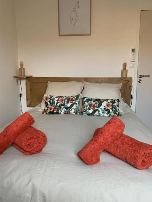 Chambre lumineuse du Mas des Ecoliers avec tête de lit en bois, oreillers à fleurs, serviettes rouges roulées et literie crème en Provence.