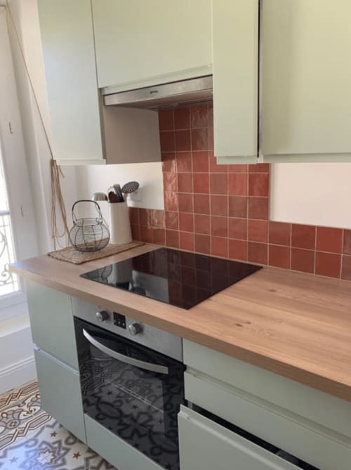Cuisine moderne avec armoires blanches, plan de travail en bois, table de cuisson à induction et dosseret en carrelage terracotta style Provence