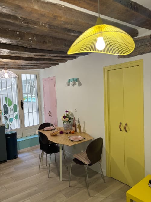Comedor de apartamento parisino moderno con lámpara colgante amarilla, vigas de madera, puertas amarillas y mesa preparada para dos personas