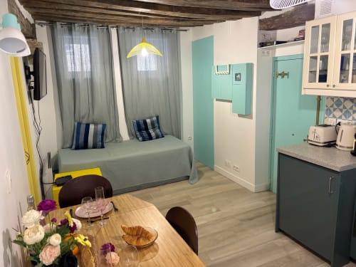 Acogedor apartamento parisino en Saint-Germain con cocineta turquesa, cama con cojines a rayas, comedor y vigas de madera