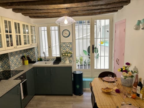 Cocina parisina moderna con armarios verde salvia, vigas de madera expuesta y comedor con flores y vino