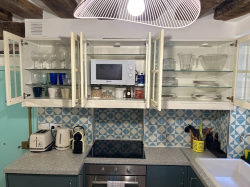 Pequeña cocina parisina moderna en ALDARO con armarios blancos, azulejos geométricos, microondas y vajilla organizada