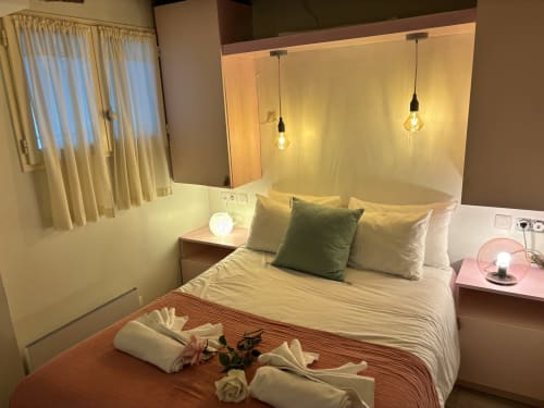Acogedora habitación de apartamento parisino con luces colgantes, almohadas verdes y amenidades de bienvenida romántica en el hotel Aldaro.