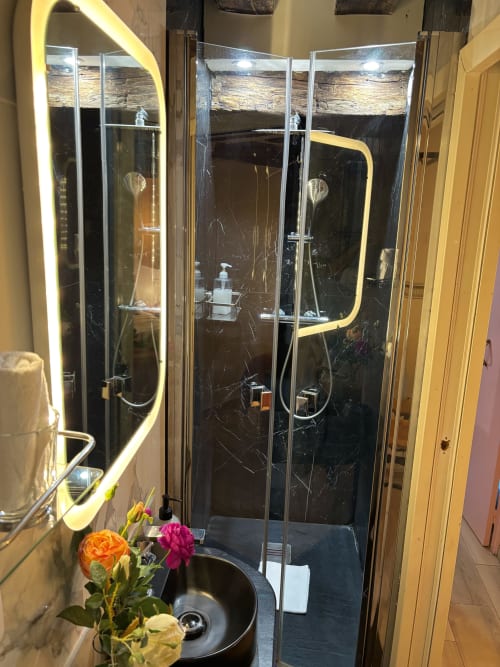 Elegante mampara de ducha en mármol negro con iluminación neón en baño de apartamento parisino, con herrajes cromados y diseño minimalista