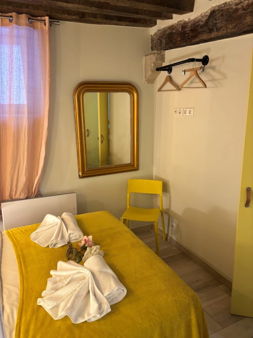Acogedor dormitorio de apartamento parisino con cama amarilla, vigas de madera, espejo dorado y encanto rústico en Saint-Germain