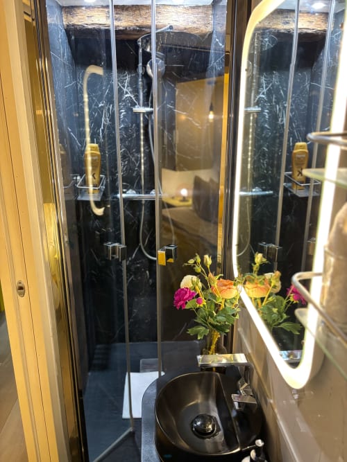 Cuarto de baño moderno en apartamento parisino con ducha de mármol negro, lavabo independiente y flores frescas en la encimera