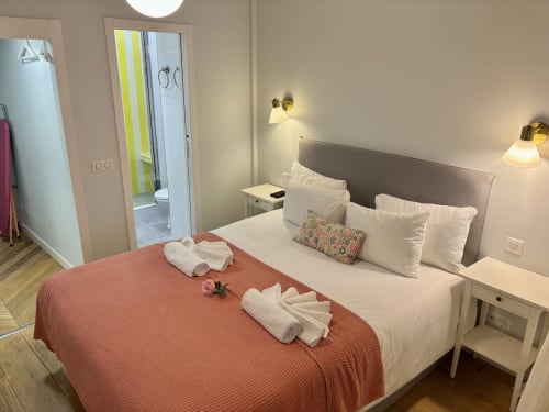 Dormitorio moderno en apartamento parisino con cama queen, manta coral, almohadas blancas, baño privado e iluminación ambiental