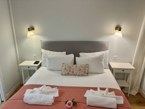 Dormitorio moderno en apartamento parisino con cabecera gris, almohadas blancas, mesitas de noche gemelas, apliques de pared en latón y toallas dobladas