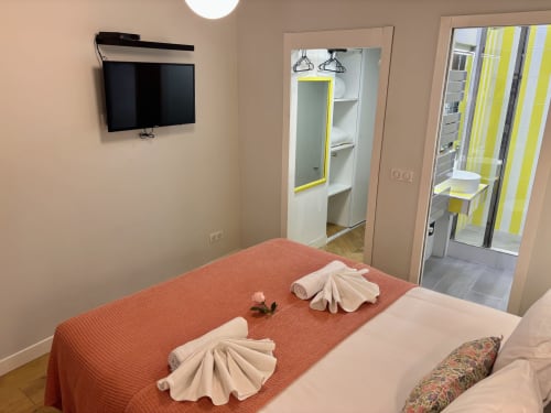 Dormitorio moderno de apartamento parisino con colcha roja, TV de pared, espejo y baño privado con acentos amarillos en el hotel Aldaro