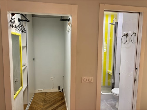 Pasillo de baño moderno en el apartamento Aldaro de París con ducha de marco amarillo y paredes de azulejos blancos