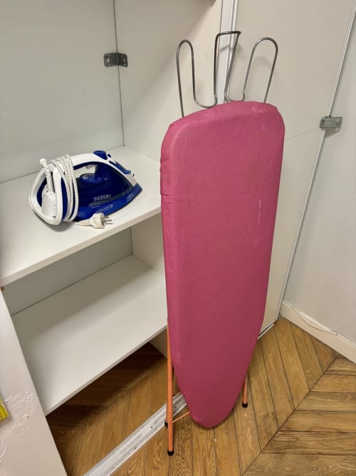 Tabla de planchar rosa con plancha guardada en estante en el área de lavandería del apartamento Aldaro Paris