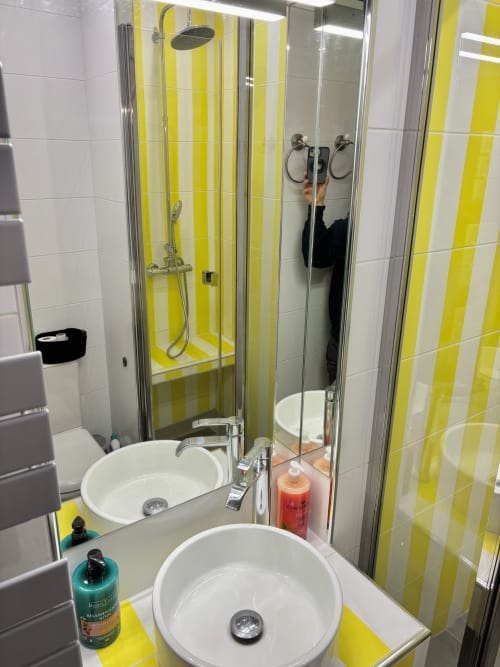 Baño moderno con doble lavamanos, azulejos amarillos y blancos a rayas, ducha de cristal en el apartamento Aldaro, París